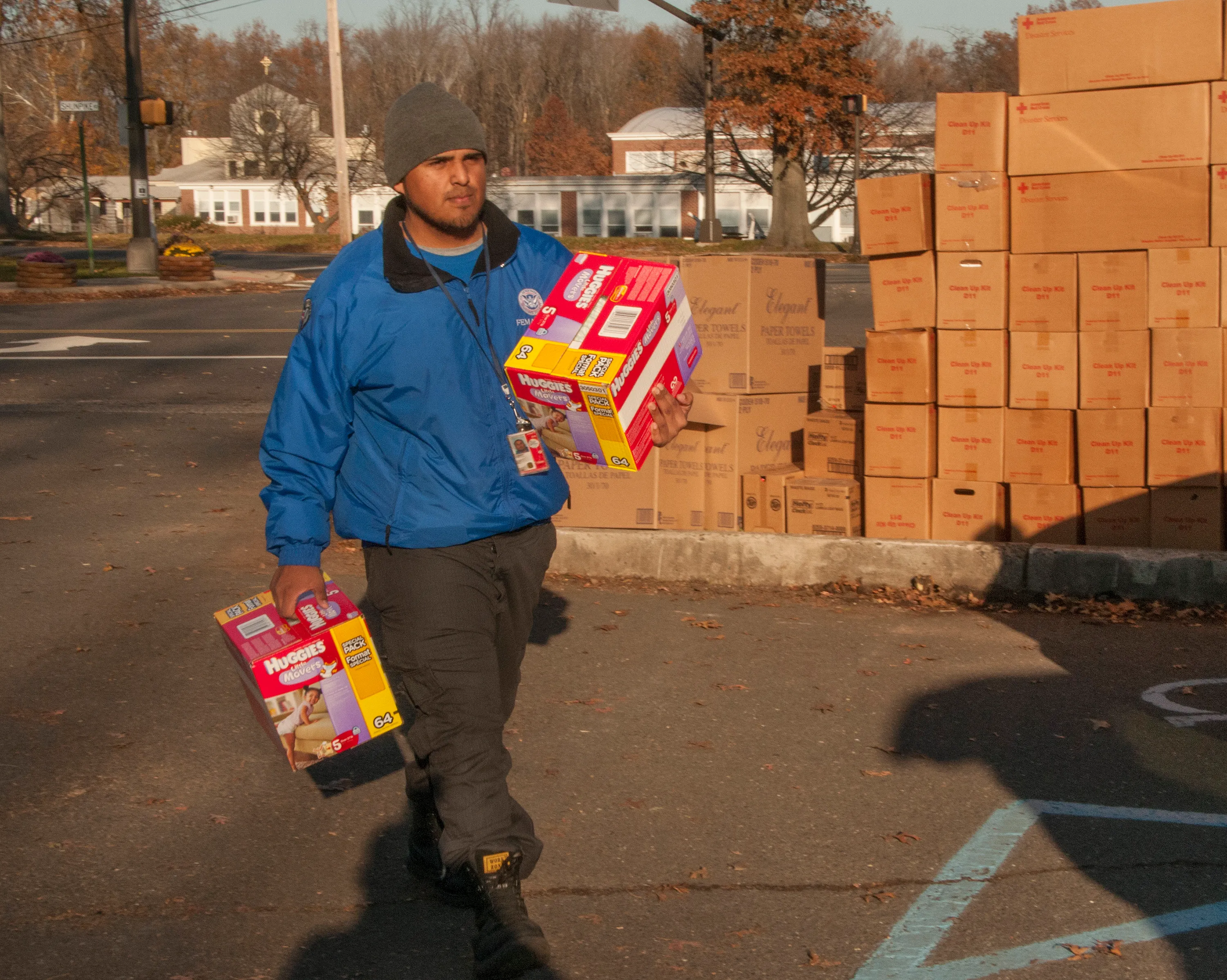 A FEMA Corps worker carrying relief supplies at a post-hurricane distribution site stacked with aid boxes