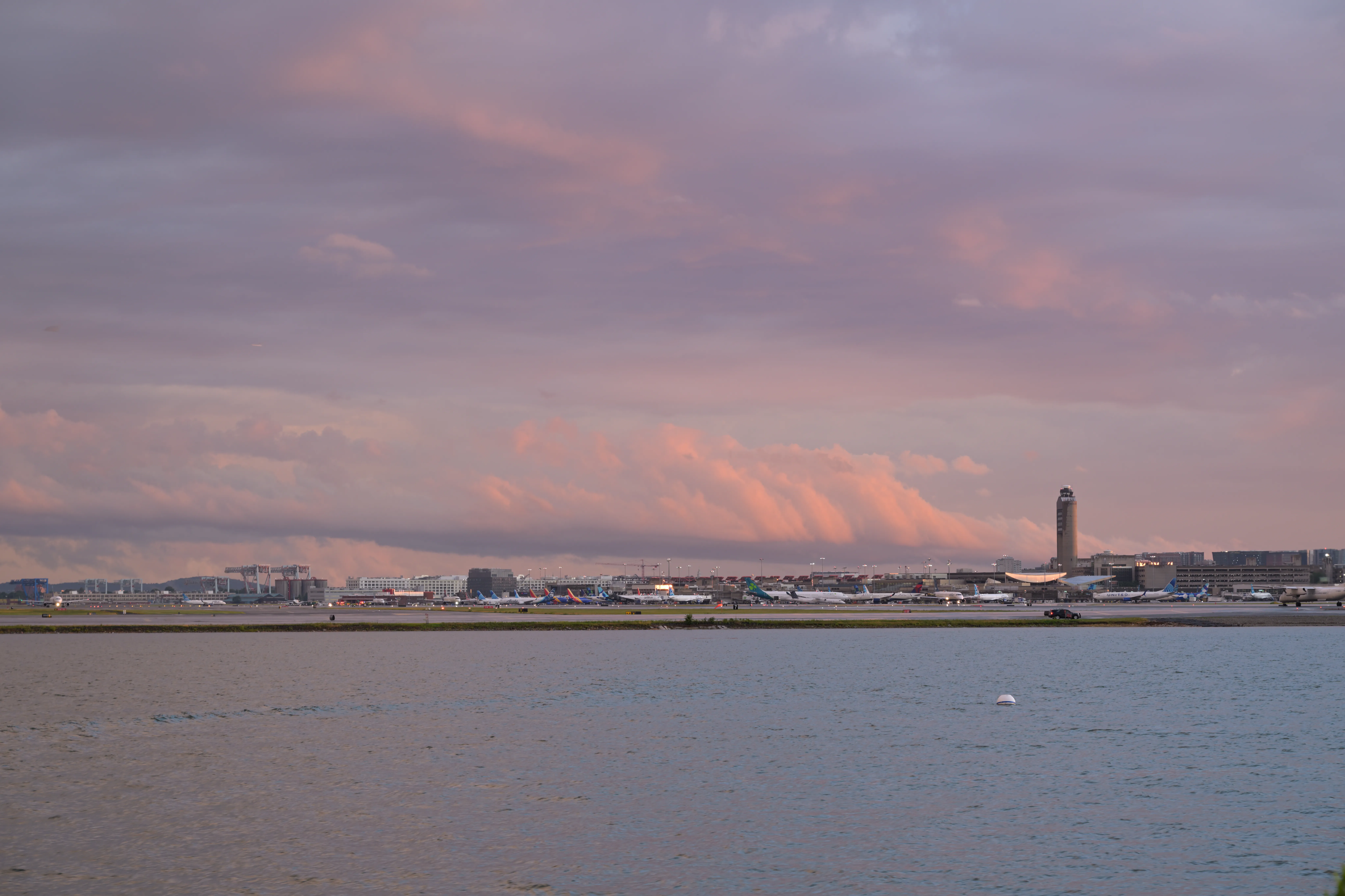 A major airport and its control tower seen across the water under clearing storm clouds