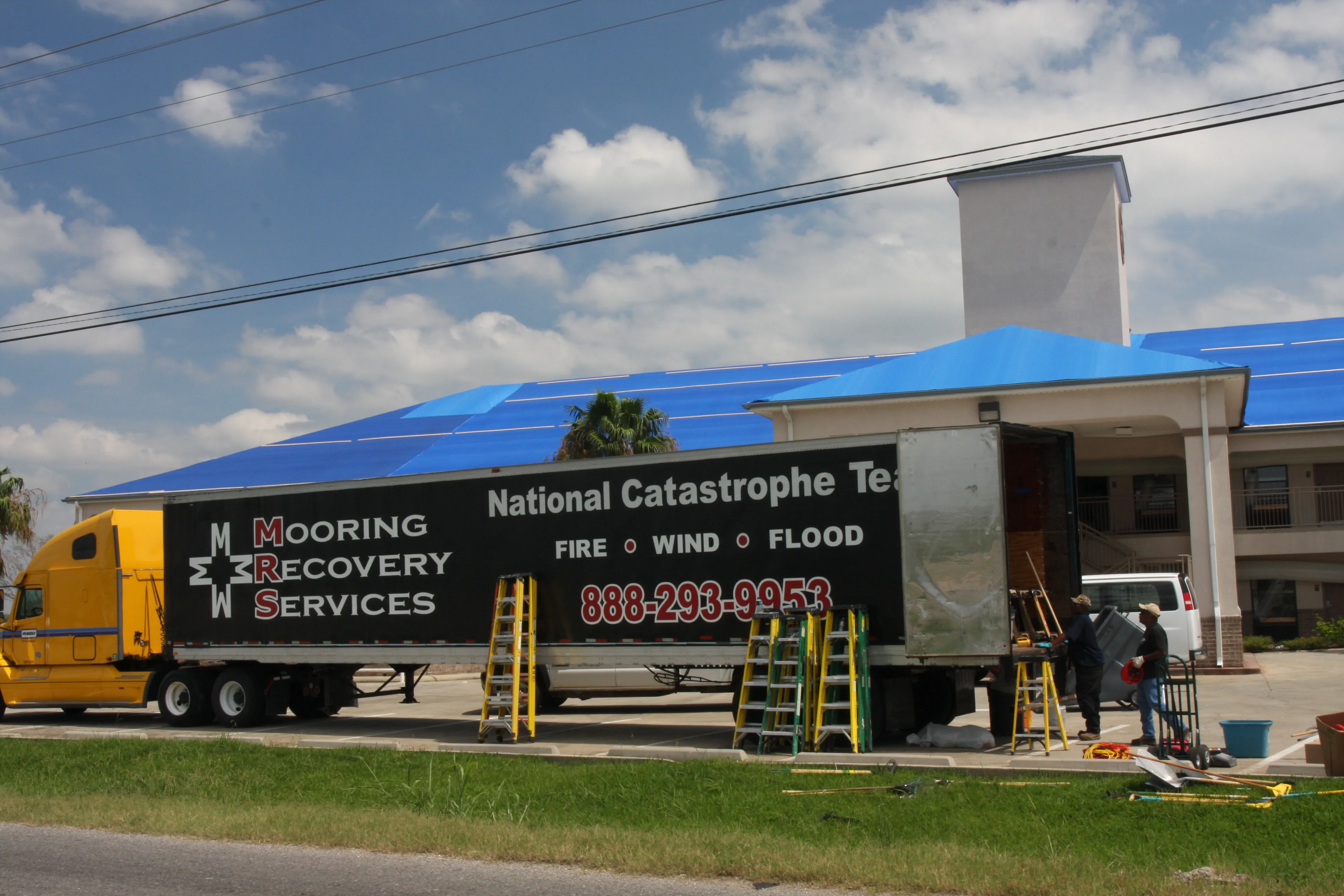 A catastrophe-restoration crew works at a motel with a blue-tarped roof after a hurricane