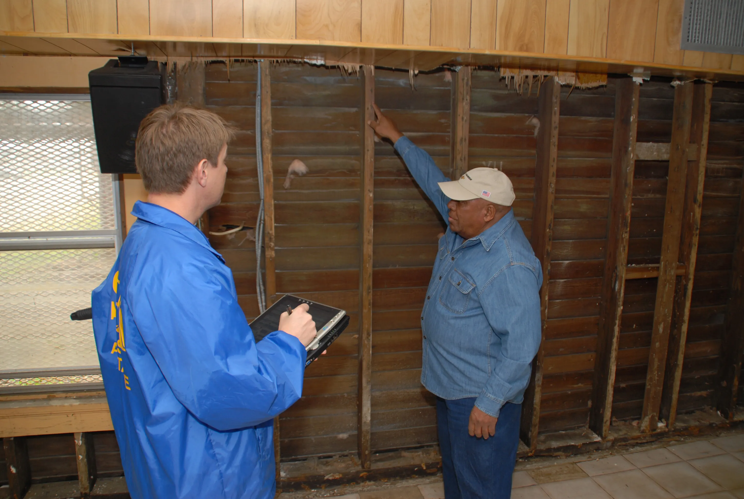 A disaster-loan inspector records the interior high-water mark as a homeowner points it out after Hurricane Katrina