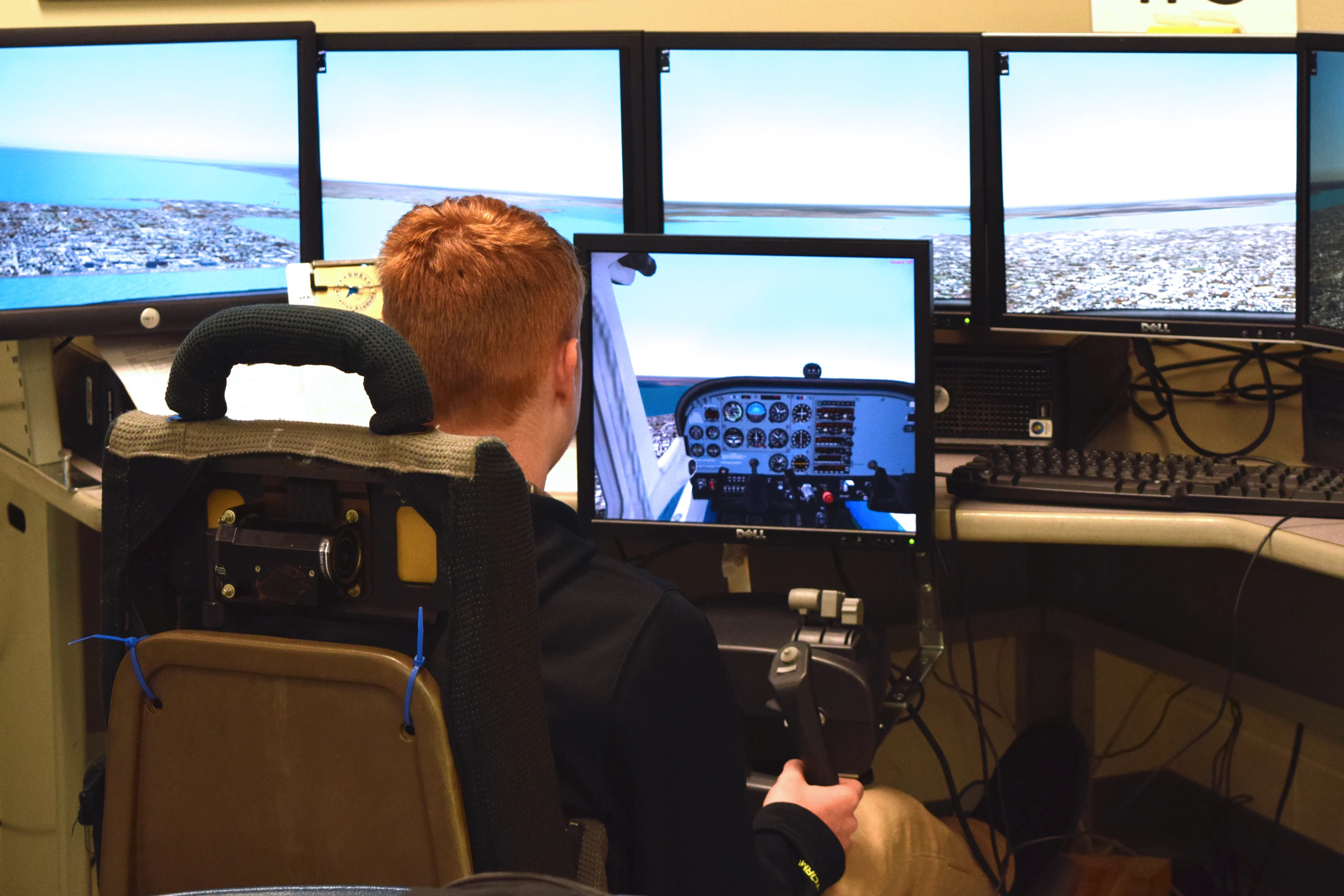 A student flies a multi-monitor desktop flight simulator showing a cockpit instrument panel