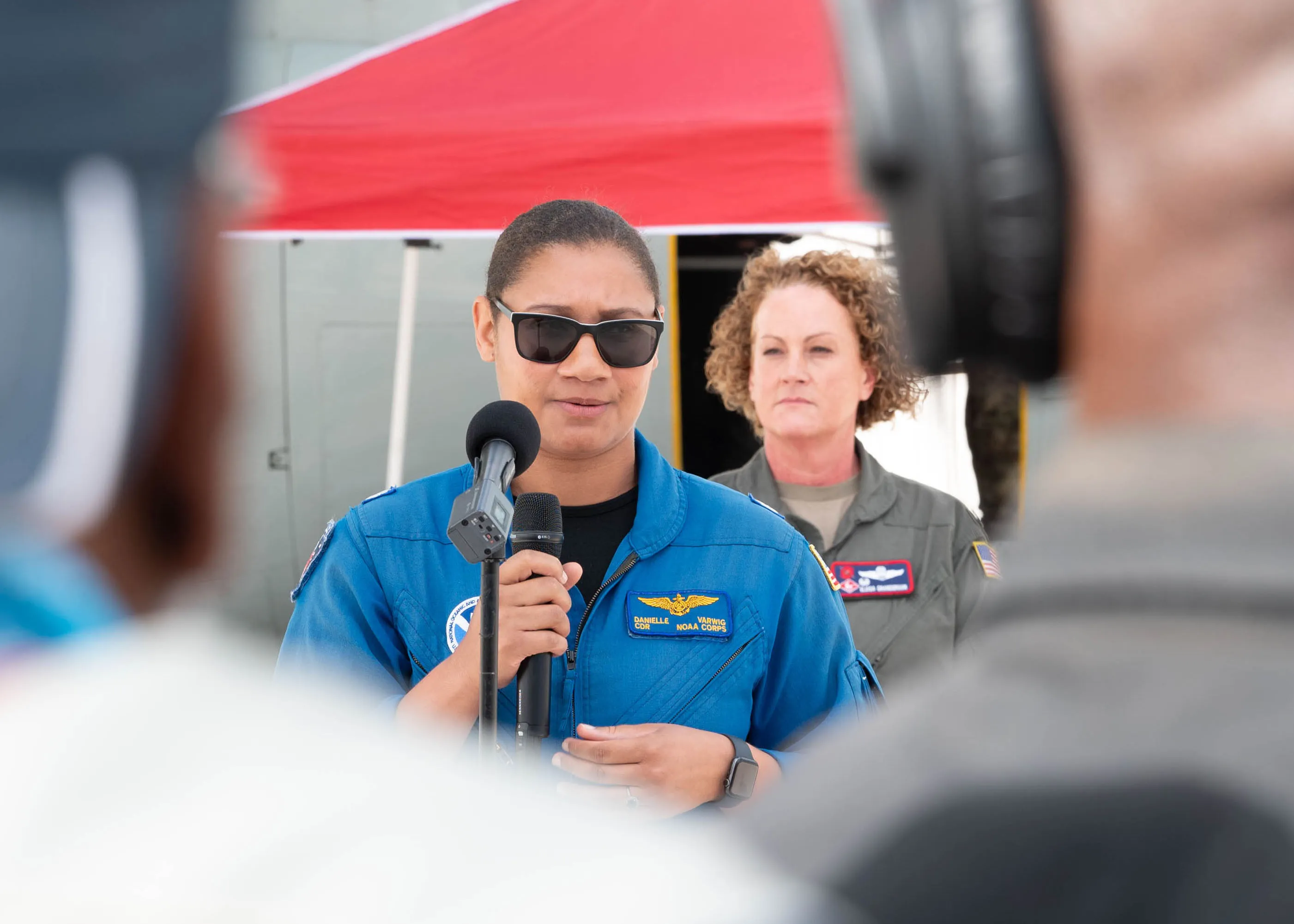 A NOAA Corps officer speaks into a microphone in front of a camera at a hurricane outreach event