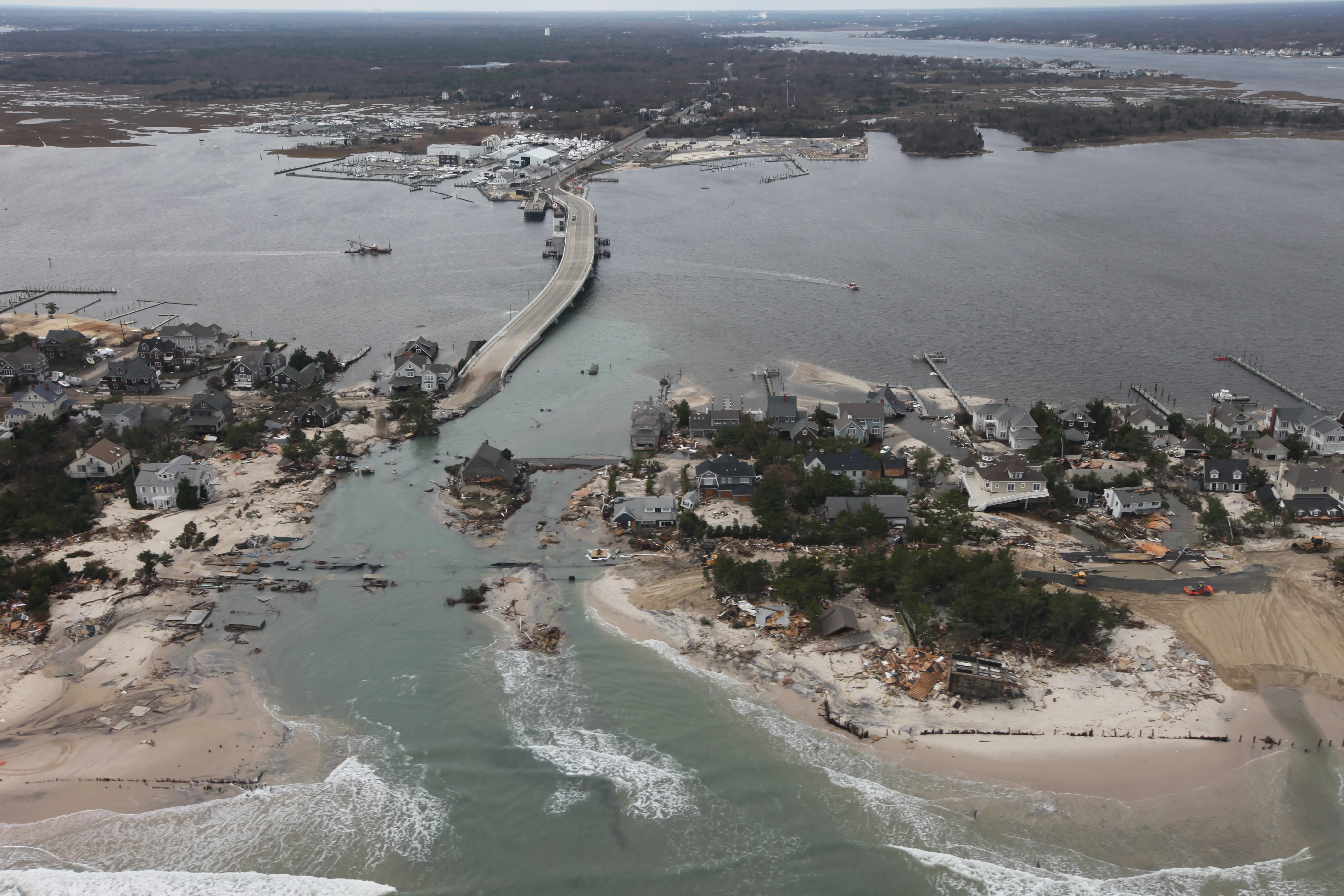 An aerial view of a barrier island cut by a new inlet, with a road and bridge severed by the breach