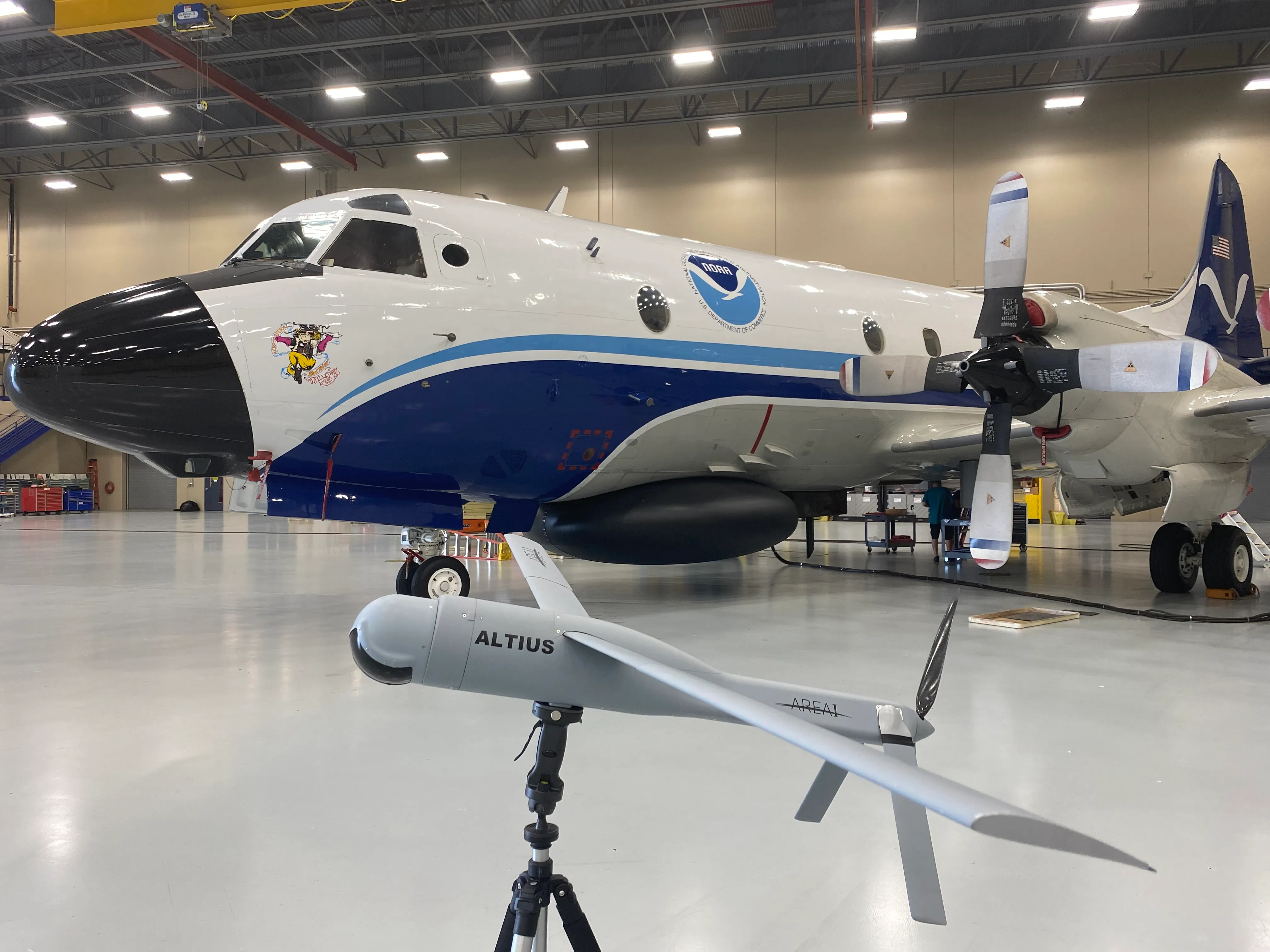 An ALTIUS uncrewed aircraft system on a stand in front of NOAA's WP-3D Orion hurricane hunter