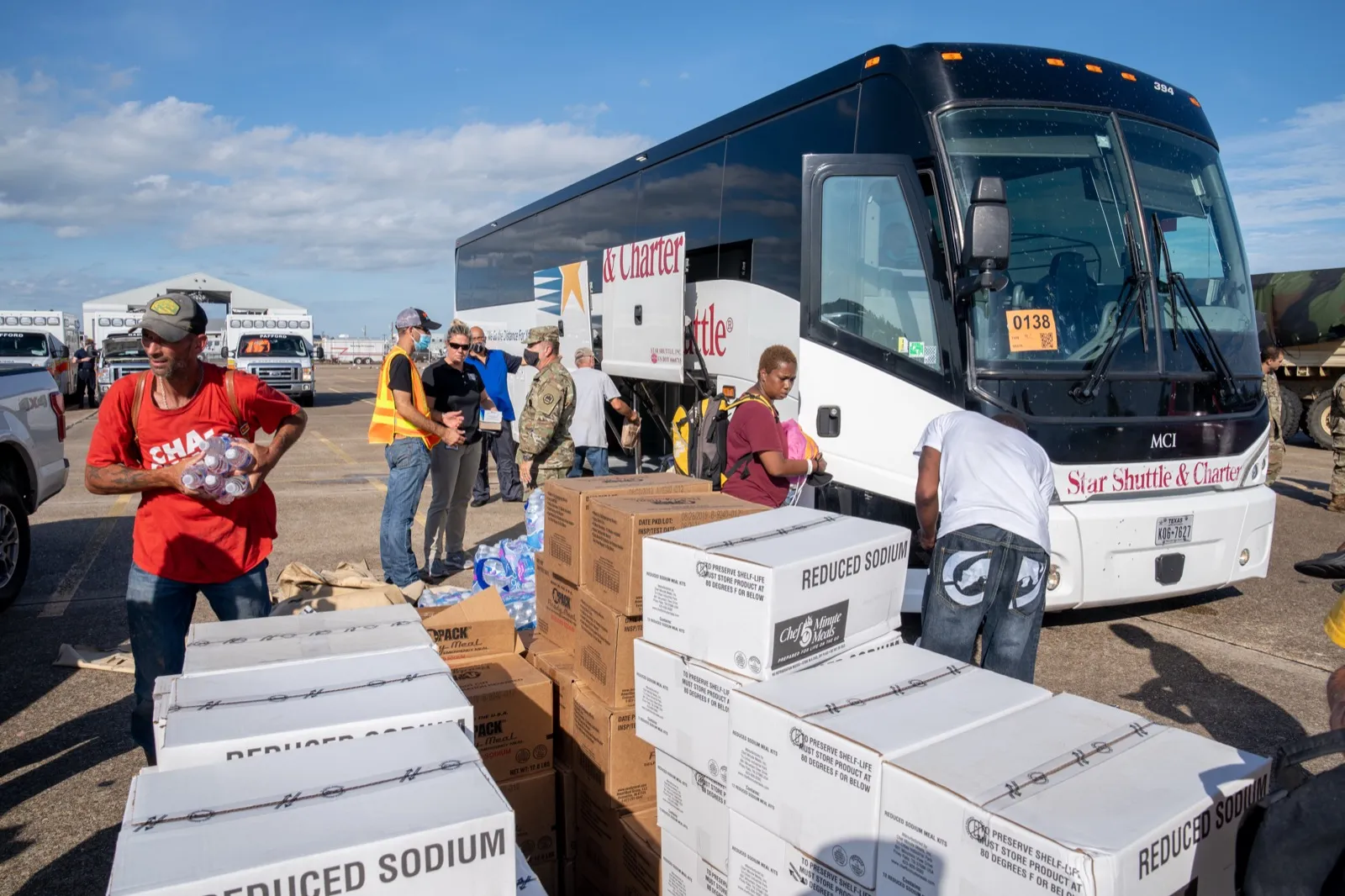 Masked evacuees and relief supplies at a bus staging area after Hurricane Laura during the COVID-19 pandemic