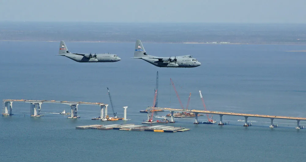 A pair of 403rd Wing C-130-family aircraft fly in formation over a coastal bay