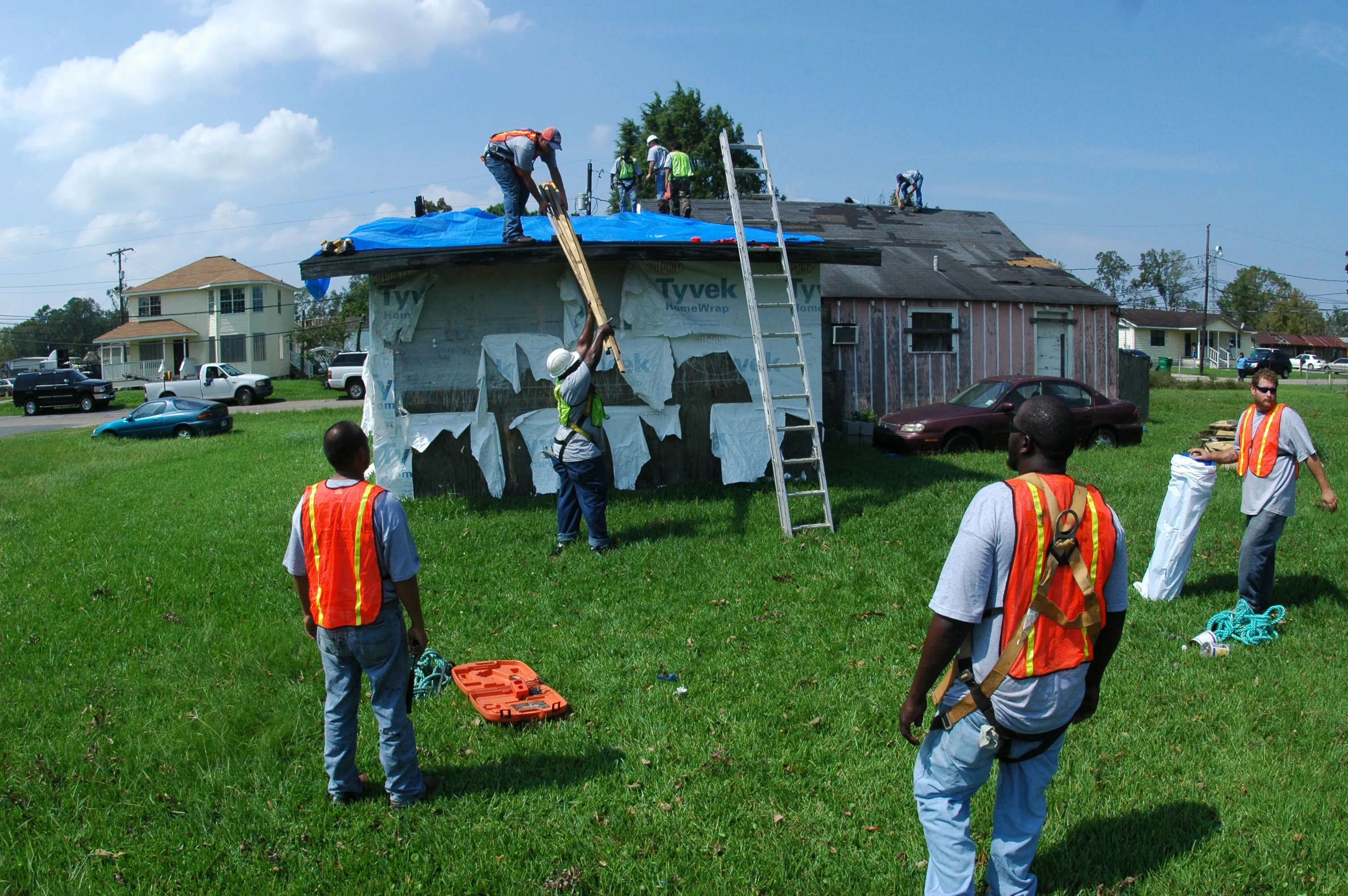 Workers installing a blue protective tarp over the damaged roof of a home after a hurricane