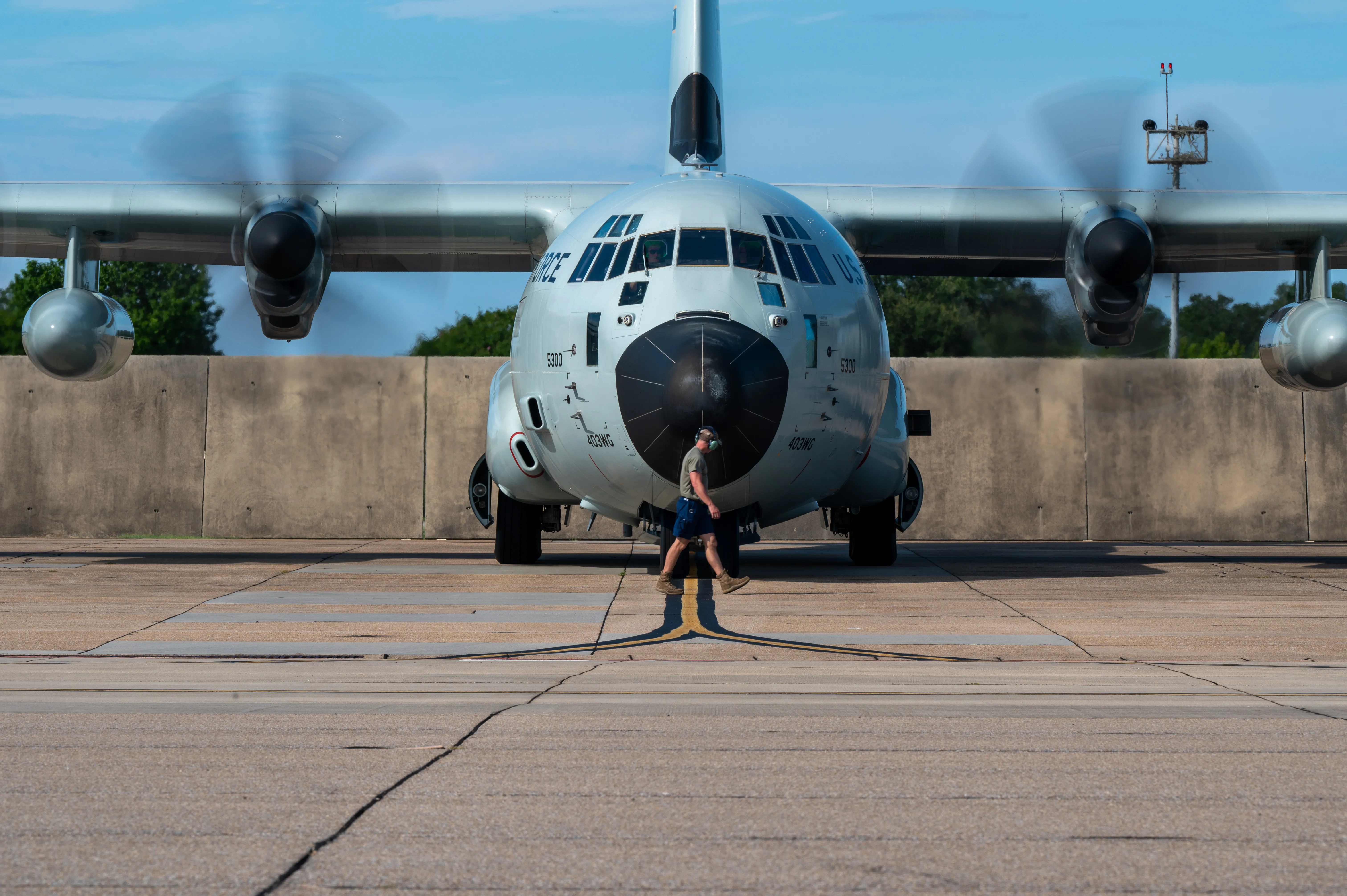 A WC-130J Hurricane Hunter with all four propellers turning as a crew member walks in front on the ramp