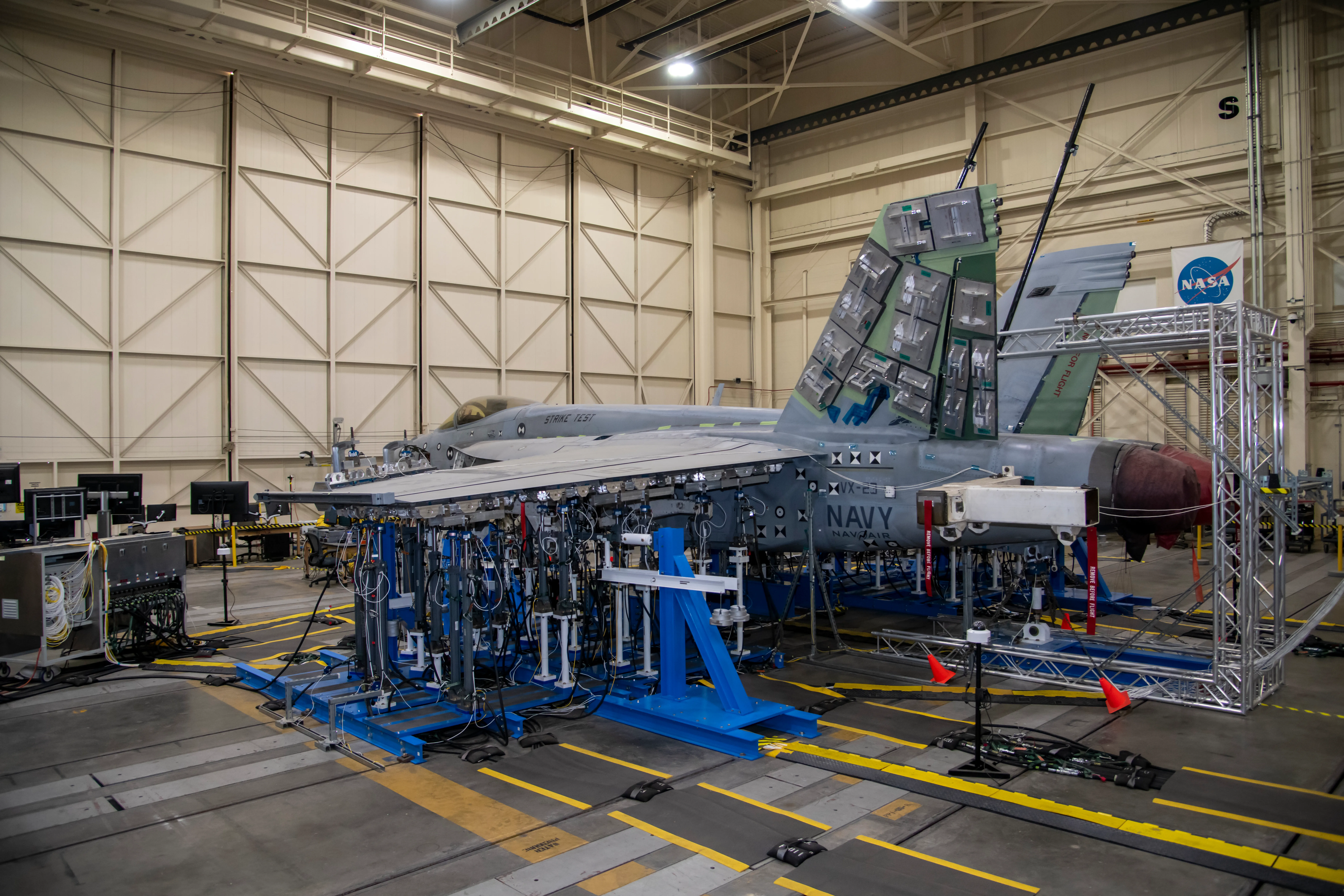 A military aircraft mounted on hydraulic jacks undergoing structural loads testing in a hangar