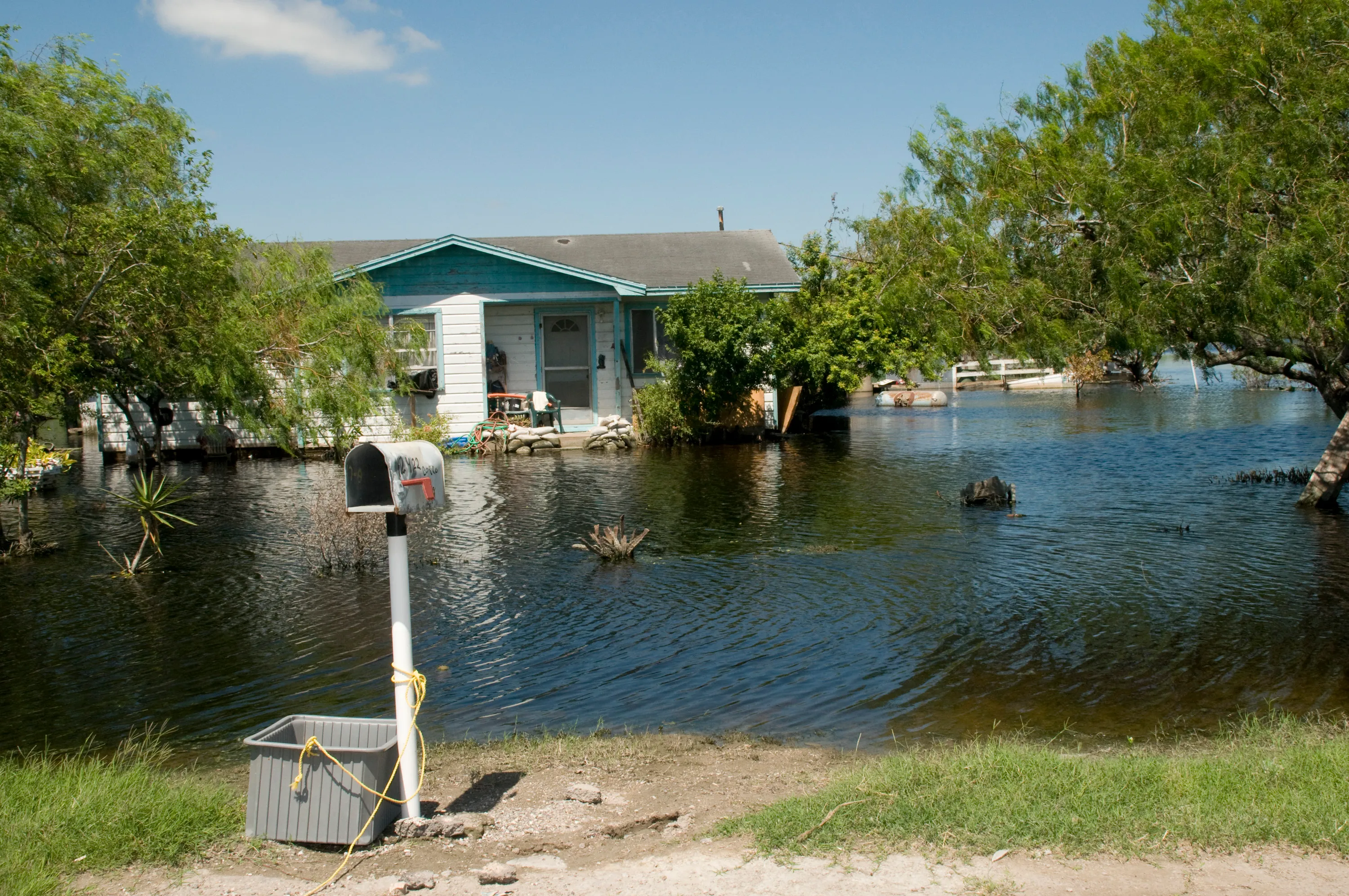 A single-story house surrounded by floodwater that has swallowed its yard and street