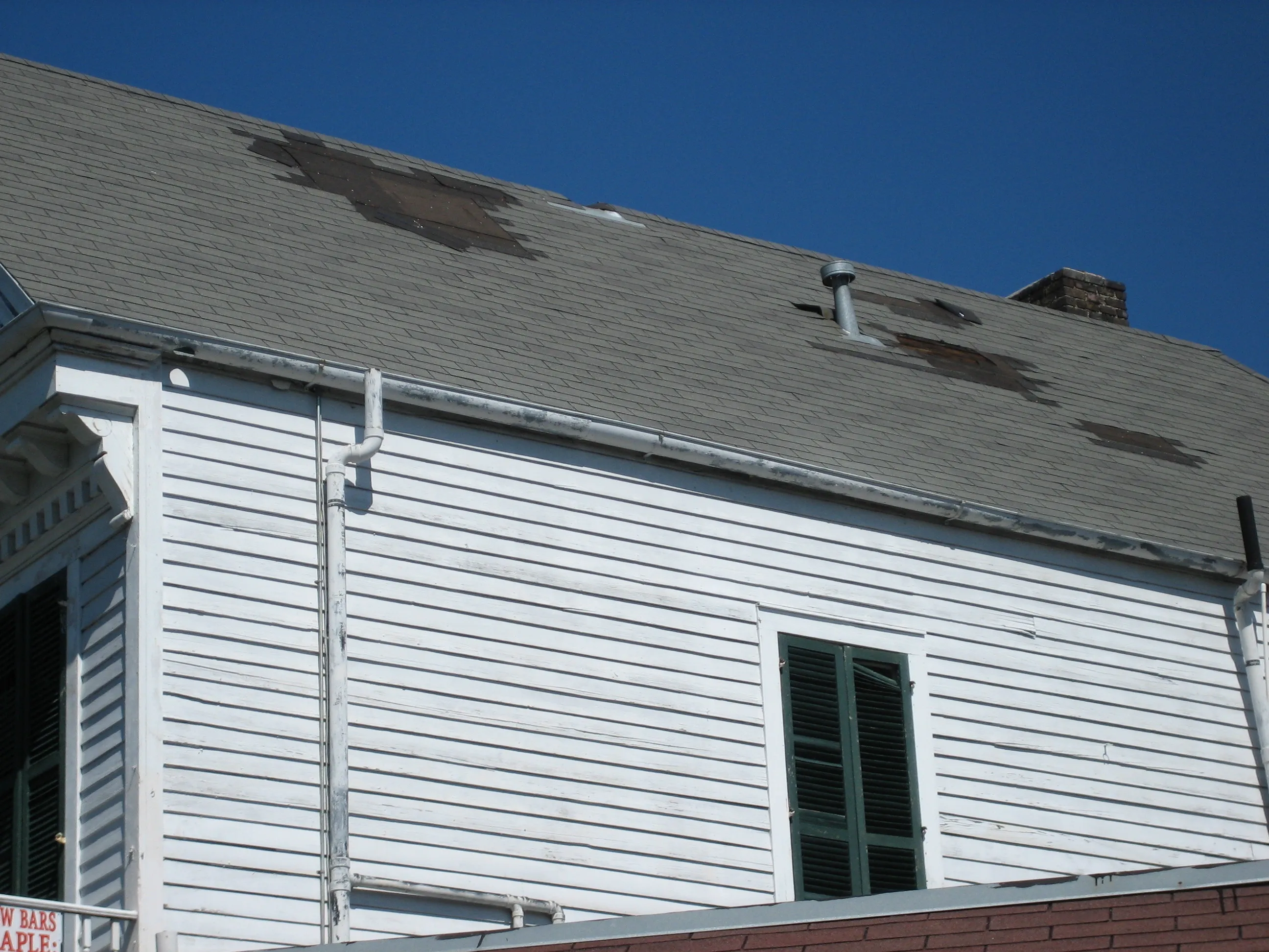 A house roof with sections of shingles and decking stripped away by hurricane winds
