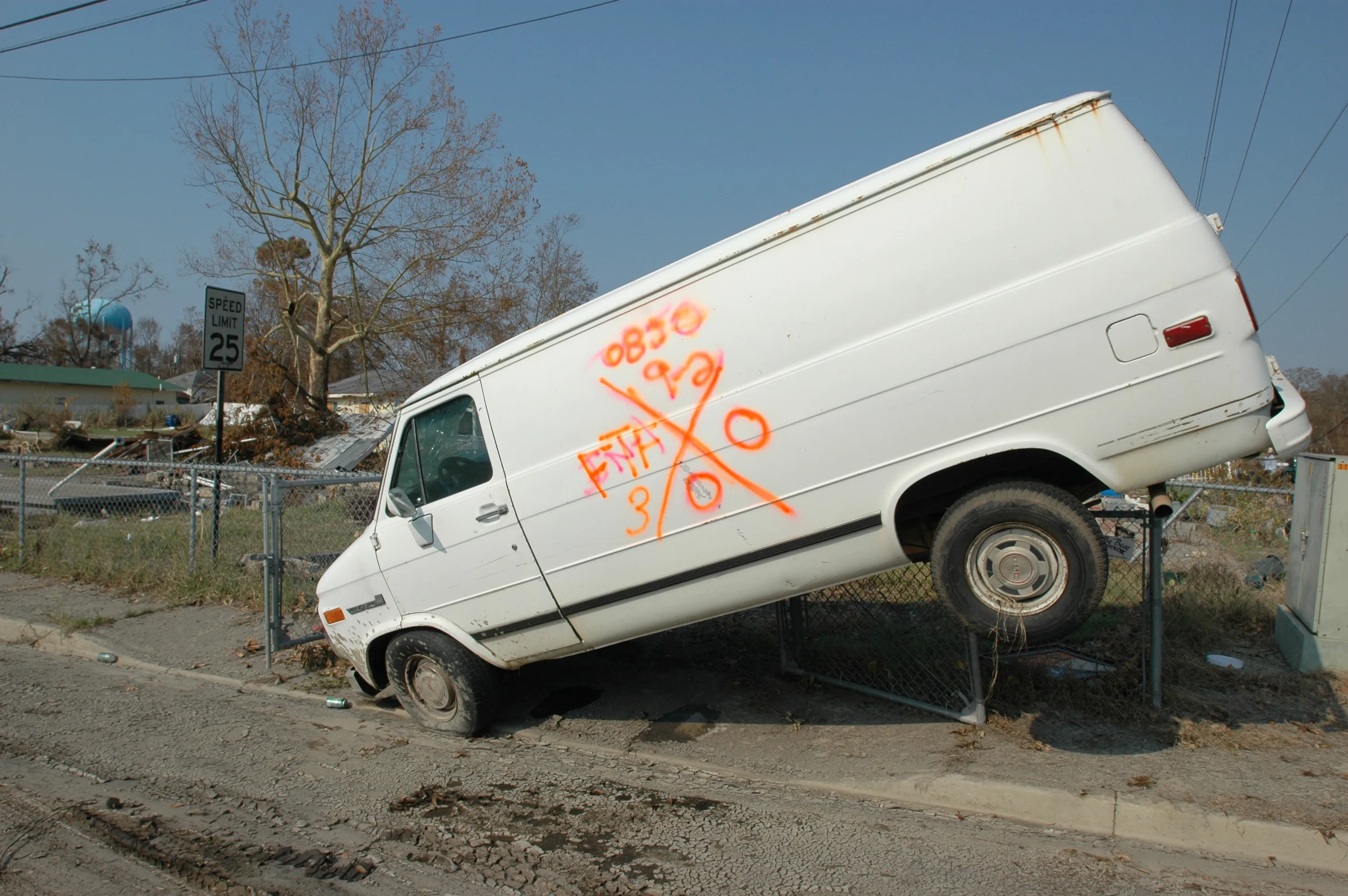 A van lifted and impaled on a chain-link fence by storm surge, marked with a search-and-rescue X