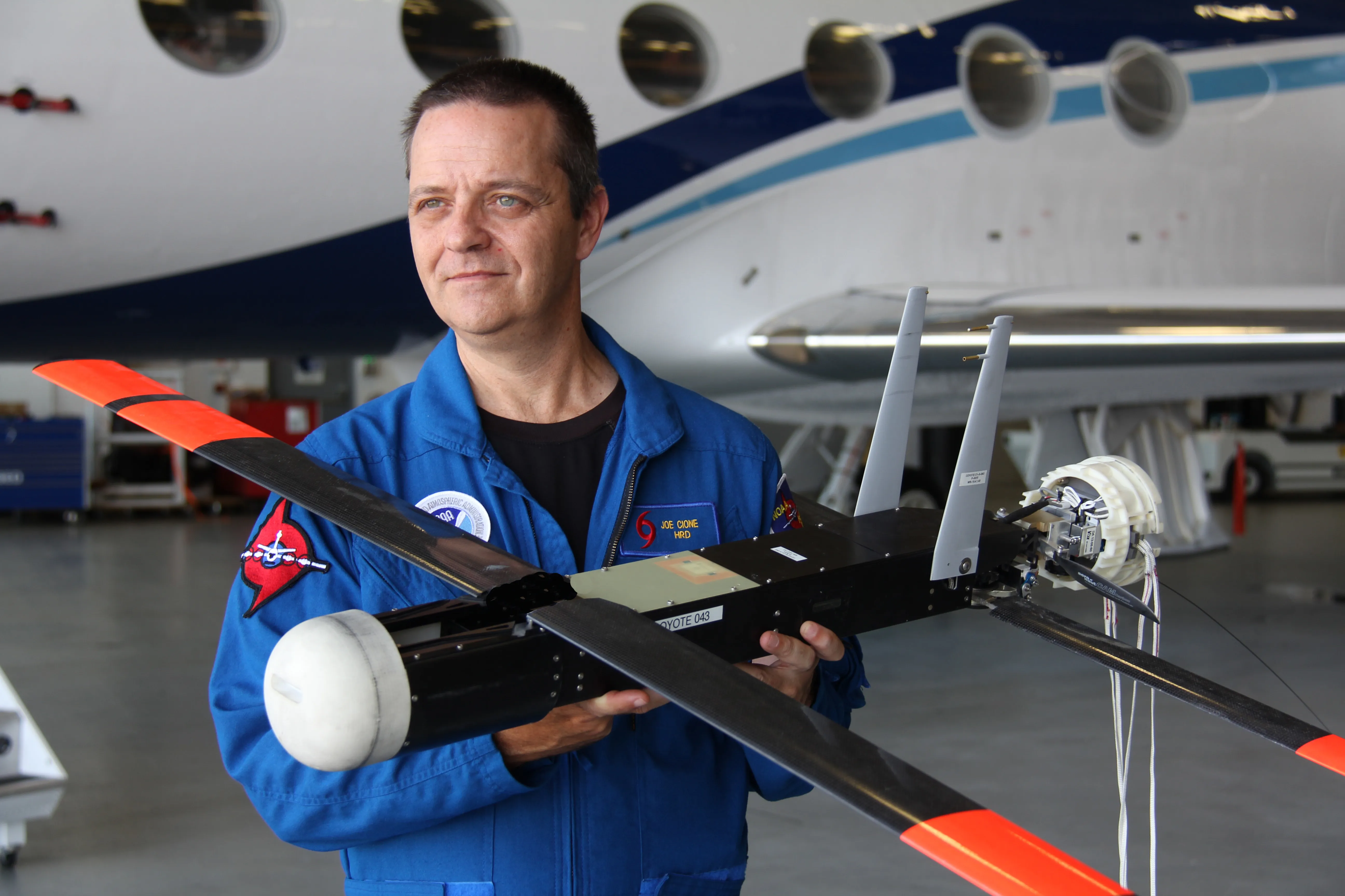 NOAA scientist Joe Cione holds a Coyote uncrewed aircraft system with folding wings in a hangar