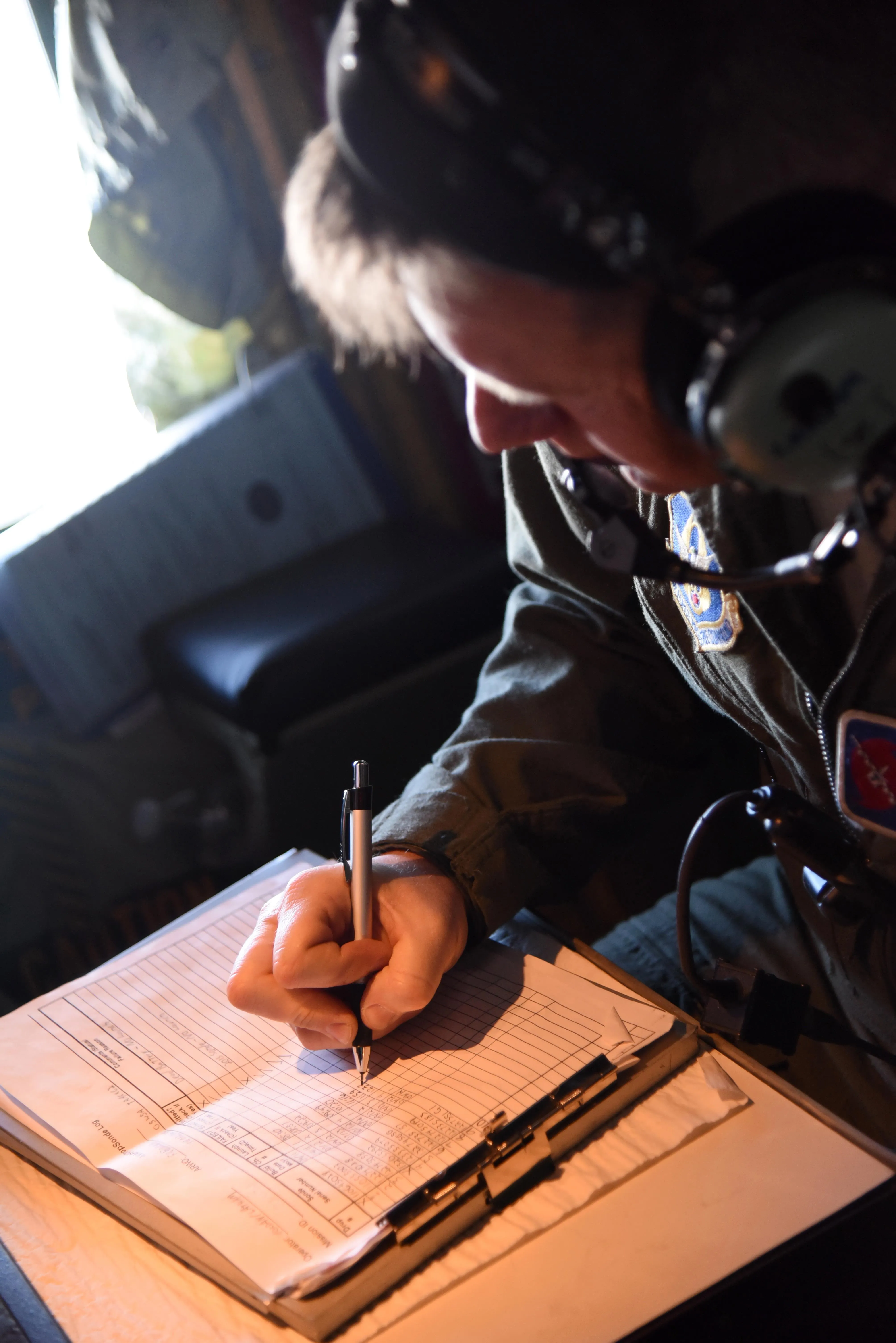 A weather reconnaissance crew member records data by hand on a clipboard aboard a Hurricane Hunter aircraft