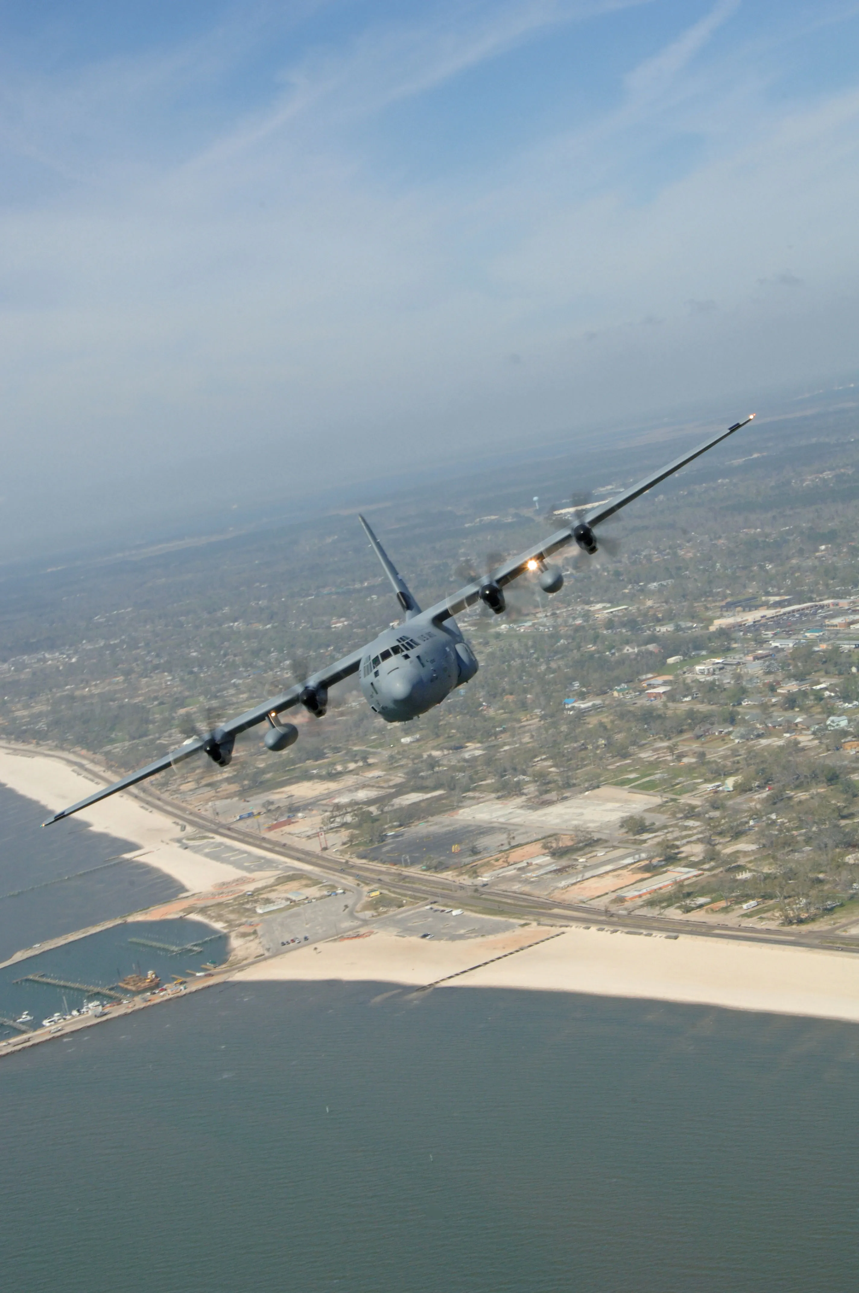 An Air Force WC-130J Hurricane Hunter banks over a storm-battered coastline