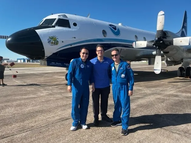 Three NOAA hurricane researchers stand on the ramp in front of a WP-3D Orion aircraft